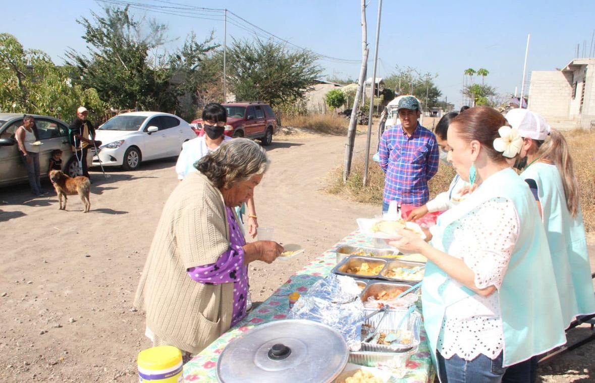 Voluntarias de Esencia del Alma sirven comida a una señora mayor en una mesa al aire libre, en una colonia de Cuautla.