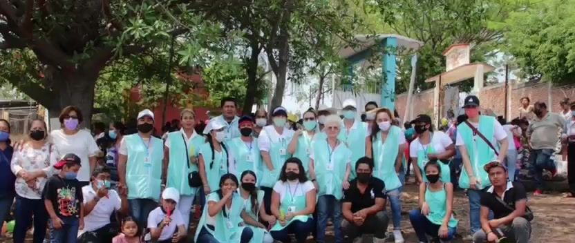 Grupo grande de voluntarias y voluntarios con chalecos color tiffany en una comunidad.